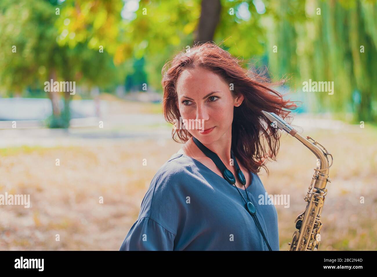 Nahes Porträt einer jungen rothaarigen Frau in einem grünen Park mit Saxofon Stockfoto