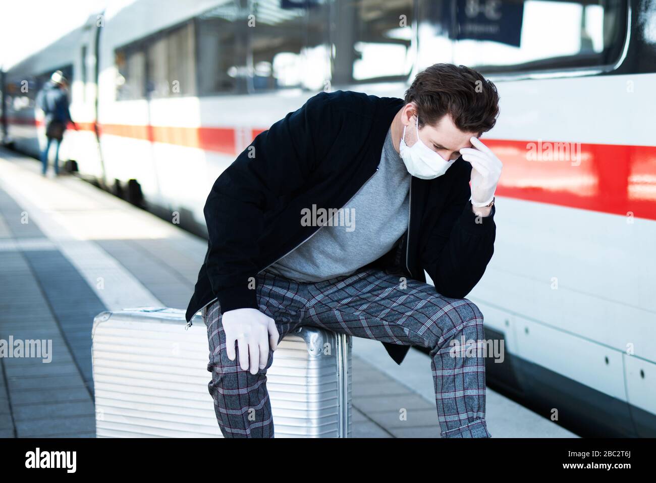 Mann mit Koffer auf der Plattform, er hat eine Gesichtsmaske und Handschuhe gegen eine Infektion mit dem Corona-Virus Stockfoto