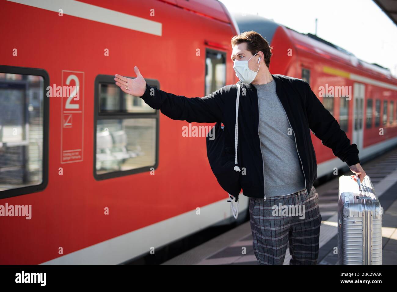 Ein Mann wartet auf einen Zug auf dem Bahnsteig, trägt eine Gesichtsmaske und Gummihandschuhe, um sich vor dem Corona-Virus zu schützen Stockfoto