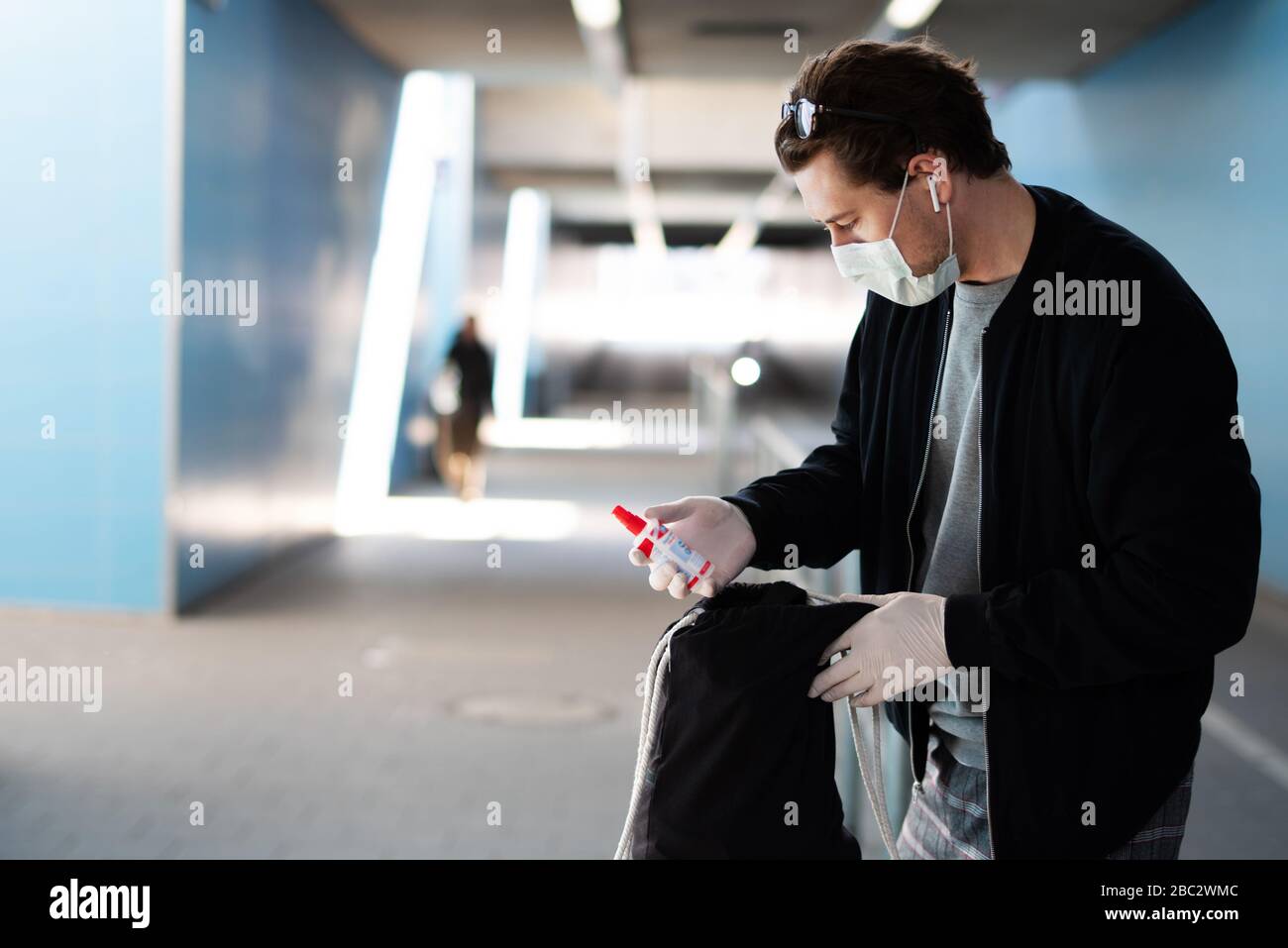 Ein Mann gehört zu einer Coronavirus-Infektion, hat eine Mundmaske, Gummihandschuhe und hat ein Desinfektionsmittel in der Hand Stockfoto