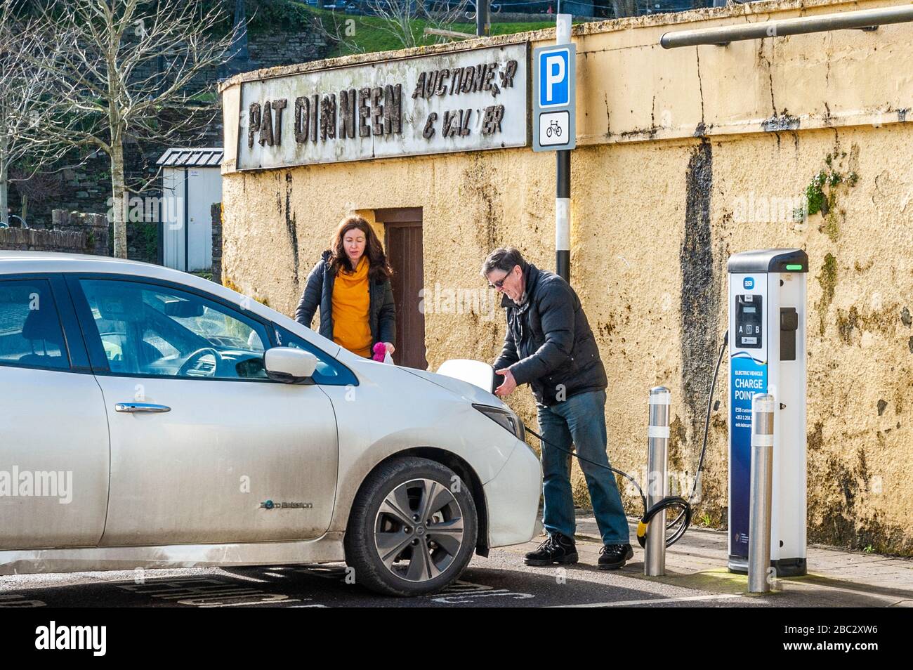 Der Mann legt ein Ladekabel von einer elektrischen Ladestation in sein Elektroauto in Irland. Stockfoto