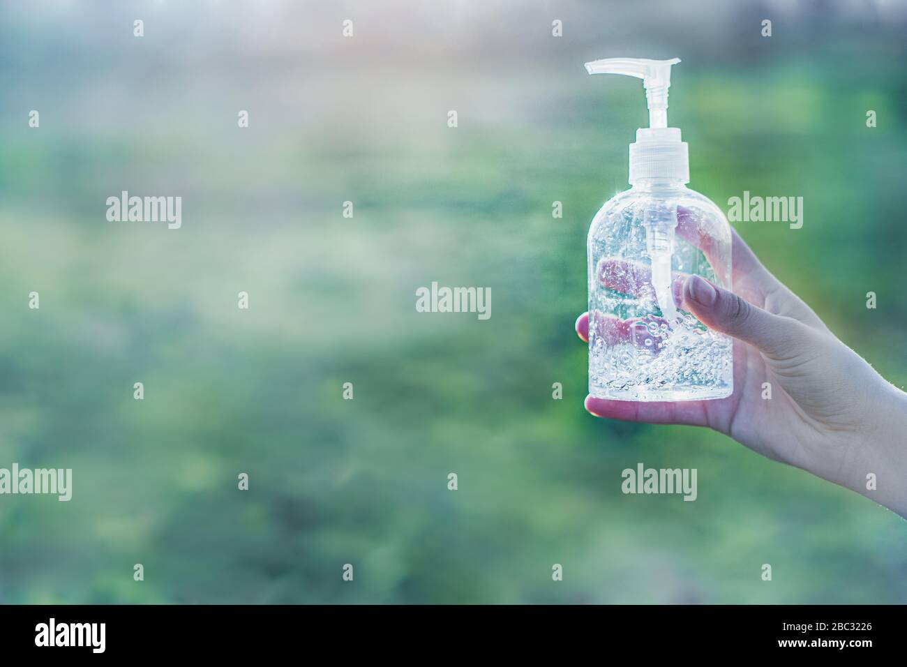 Transparente weiße Kunststoffhülle aus antibakterieller Desinfektionsflüssigkeit in den Händen mit klarem grünen Hintergrund Stockfoto