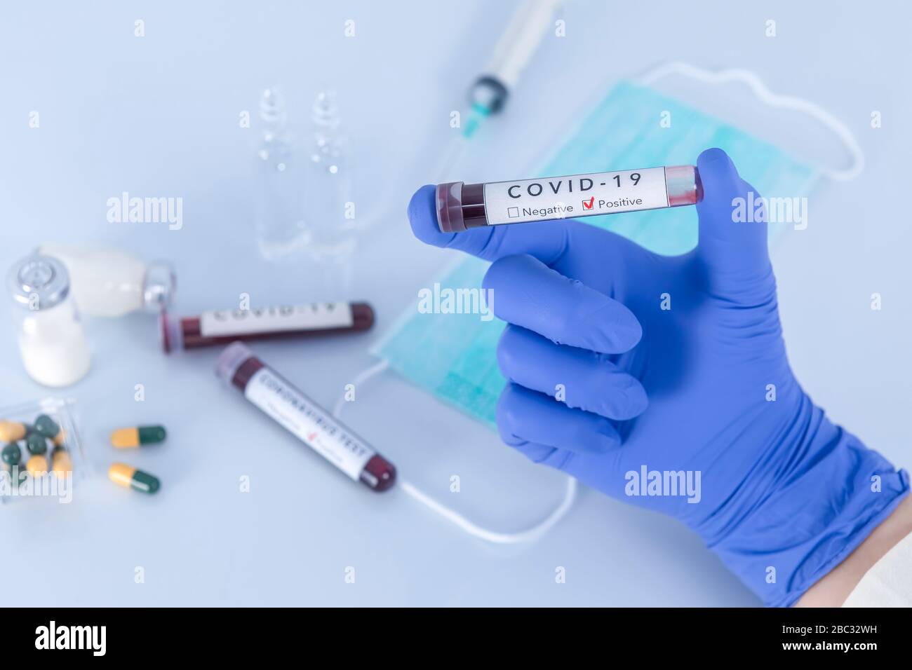Analystenhand mit Schutzhandschuhen, die COVID 19 Coronavirus Testblut halten. Virentest- und Forschungskonzept. Fokus auf Testblut. Stockfoto