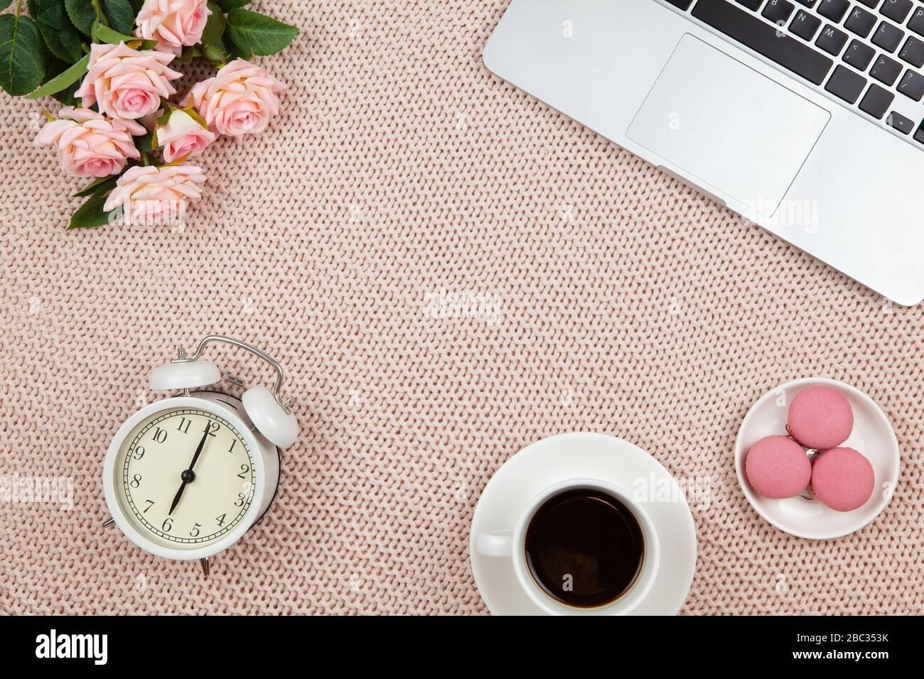 Telearbeit von zu Hause aus. Moderner weiblicher Arbeitsbereich, Draufsicht. Laptop, Kaffee, Kuchen, Rosen, Uhr auf Strickdecke, Kopierraum, flacher Lay. Schreibtisch Stockfoto