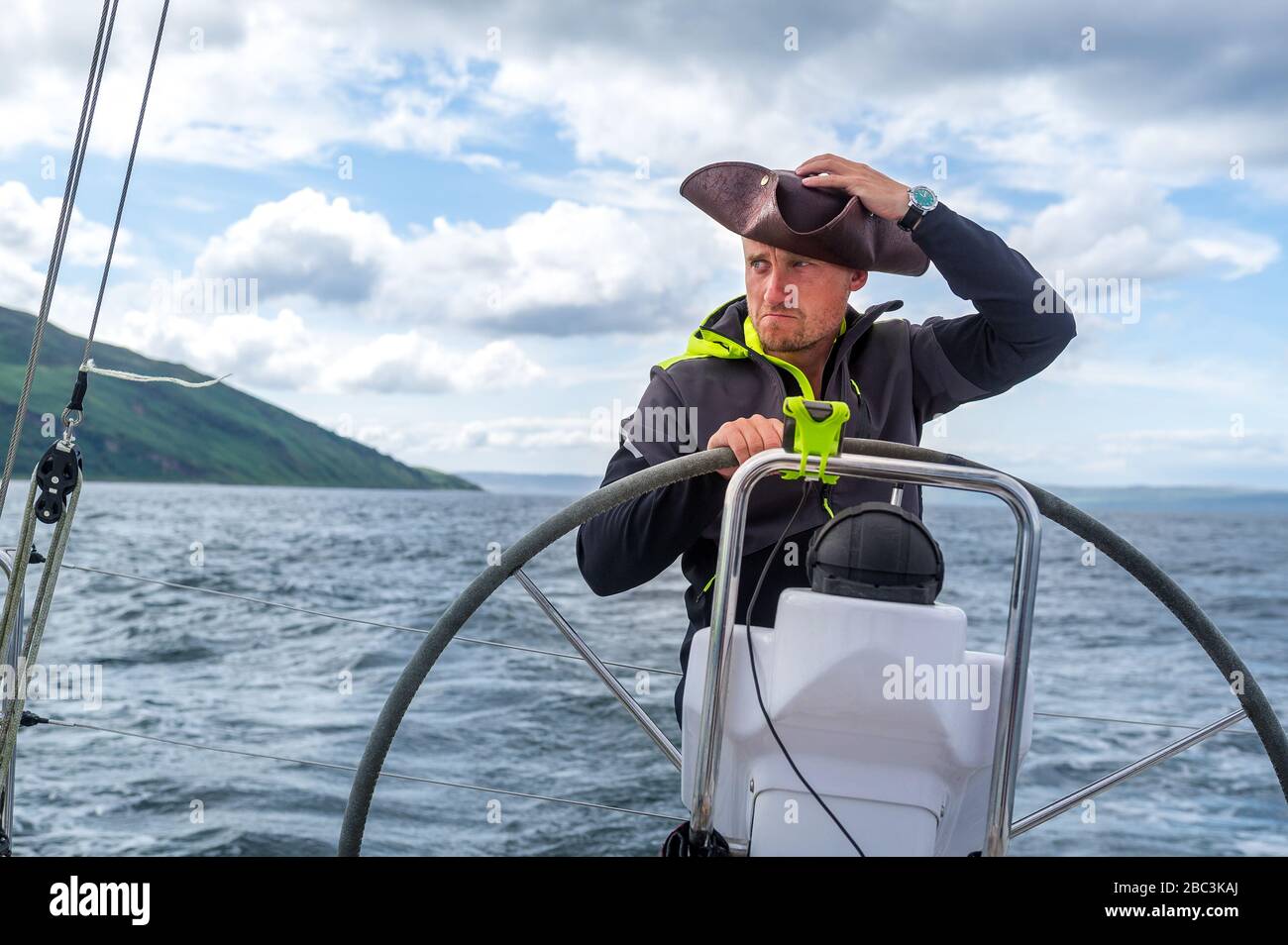 Segelboot Skipper mit Piratenstil verspotteten Hut am modernen Segelyacht-Helm. Arran Island, Schottland Stockfoto