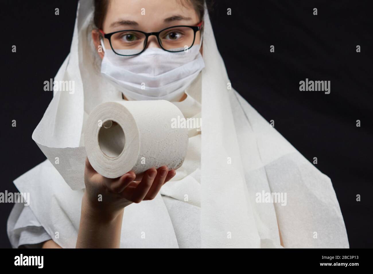 Ein gieriger Jugendlicher mit Brille und einer Maske, die in toilettenrollen gewickelt ist. Stockfoto