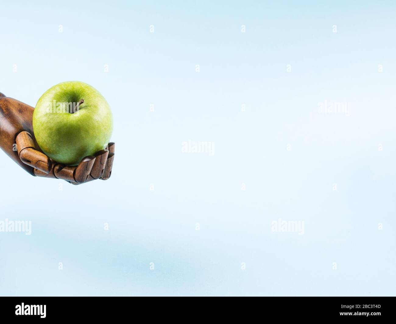 Frischer grüner apfel in der Palme aus Holzhand auf Blau Stockfoto