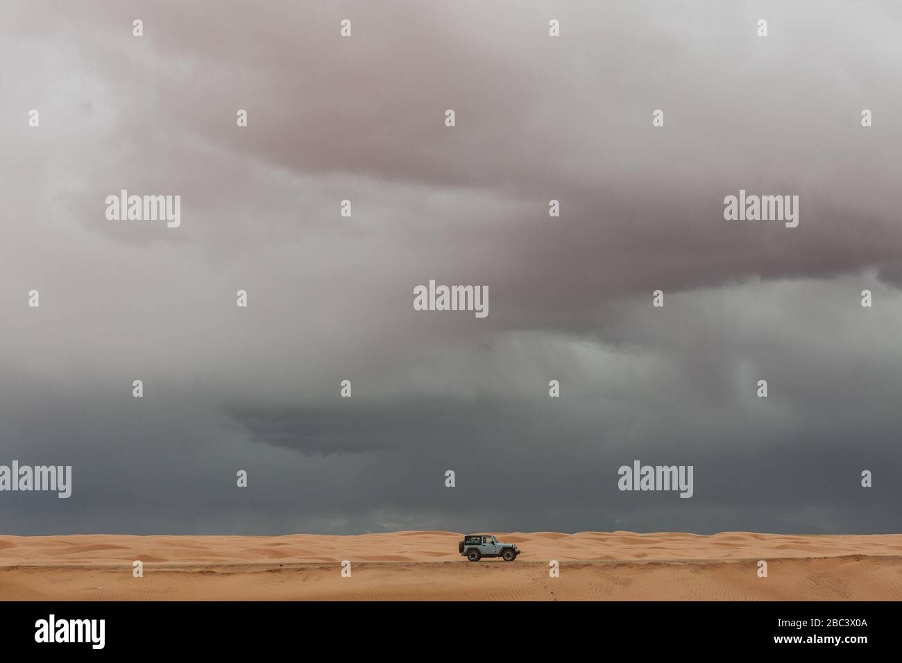 Baby Blue Jeep fährt auf Sanddünen der utah Wüste unter stürmischem Himmel Stockfoto