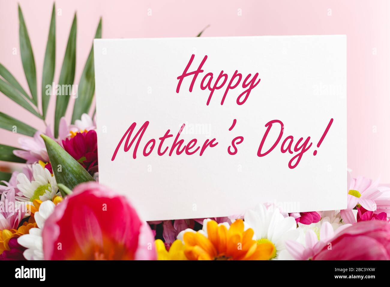Happy Mothers Day Text auf Geschenkkarte in Blumenstrauß auf pinkfarbenem Hintergrund. Grußkarte für Mama. Blumenlieferung, Glückwunschkarte in Blumen für Stockfoto