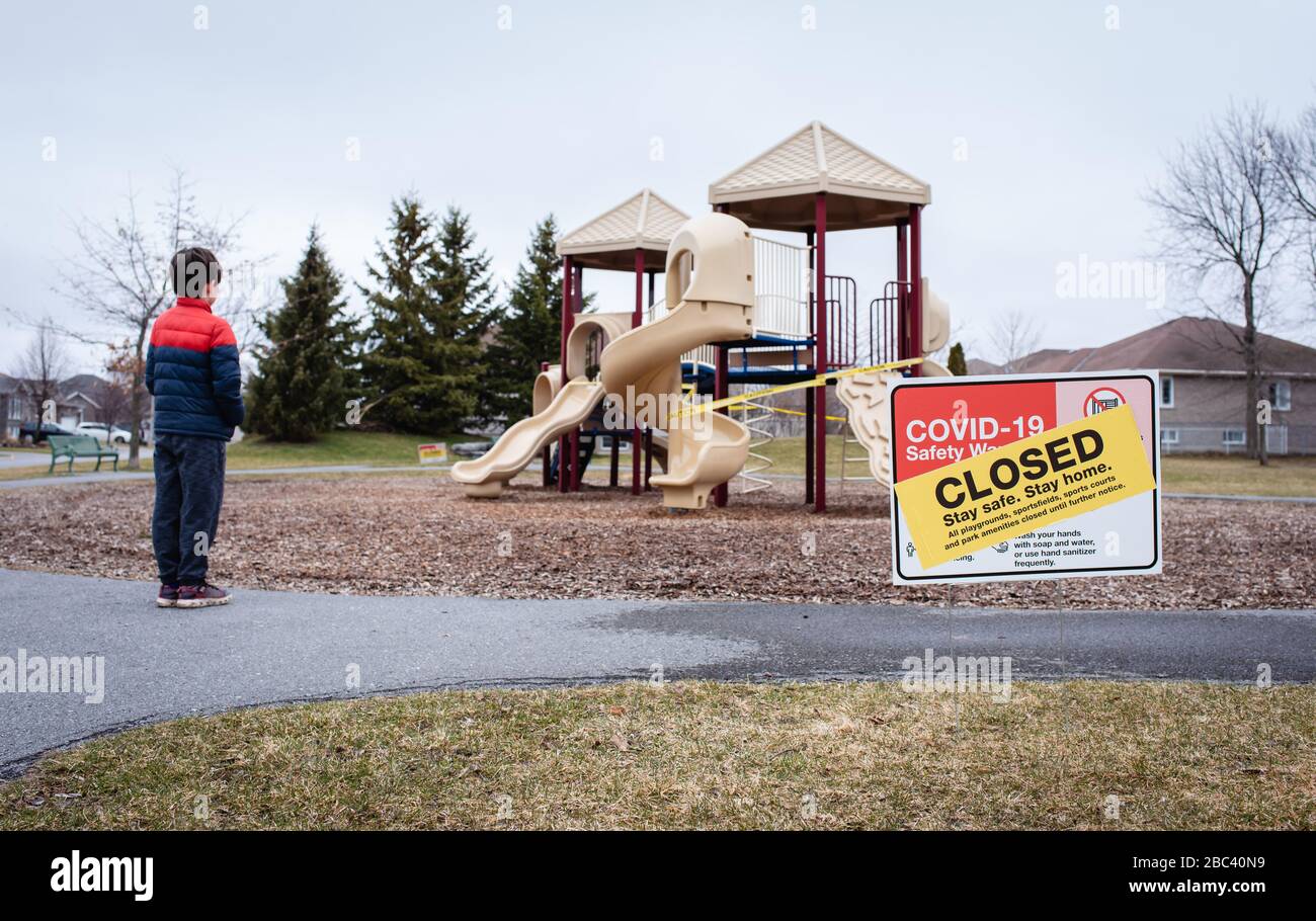 Kleiner Junge, der während der Covid 19-Pandemie auf einen geschlossenen Spielplatz schaut. Stockfoto