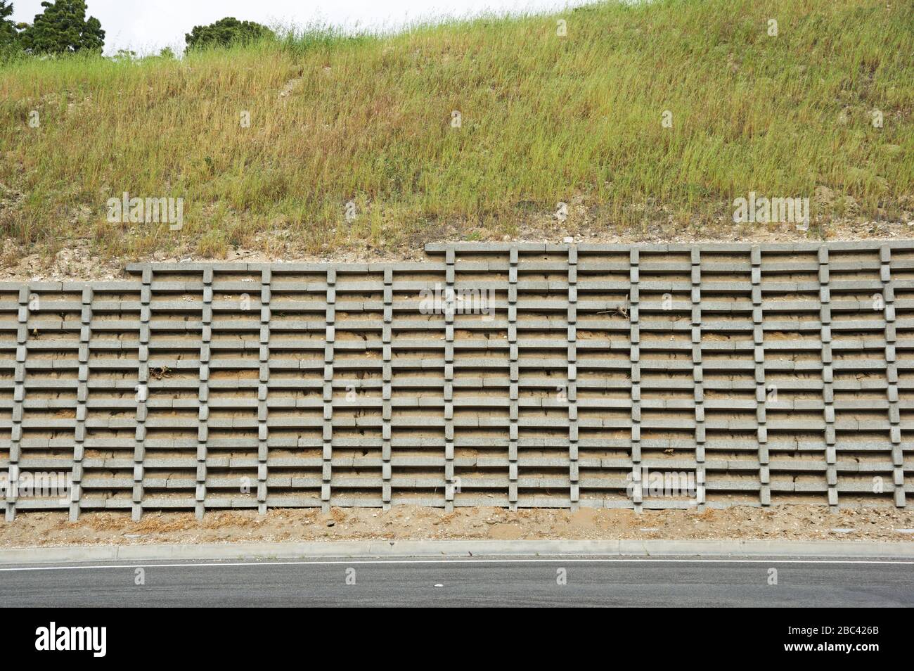 Betonkrippe, die die Wand mit grasbewachsenem Gefälle darüber schützt, schützt eine Straße Stockfoto