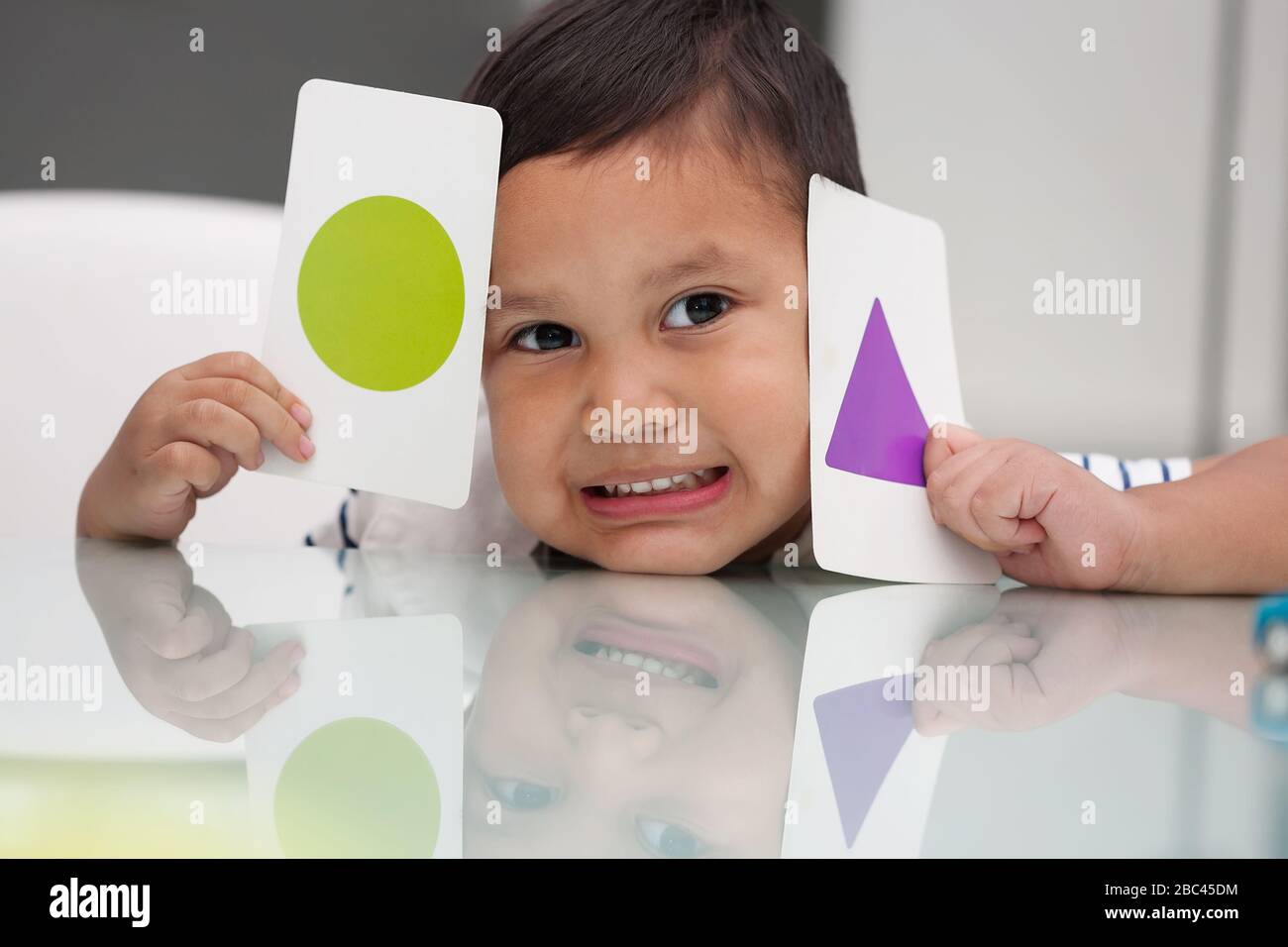 Kleiner Junge, der Flash-Karten hält, um mehr über grundlegende Formerkennung und Farben zu erfahren. Stockfoto