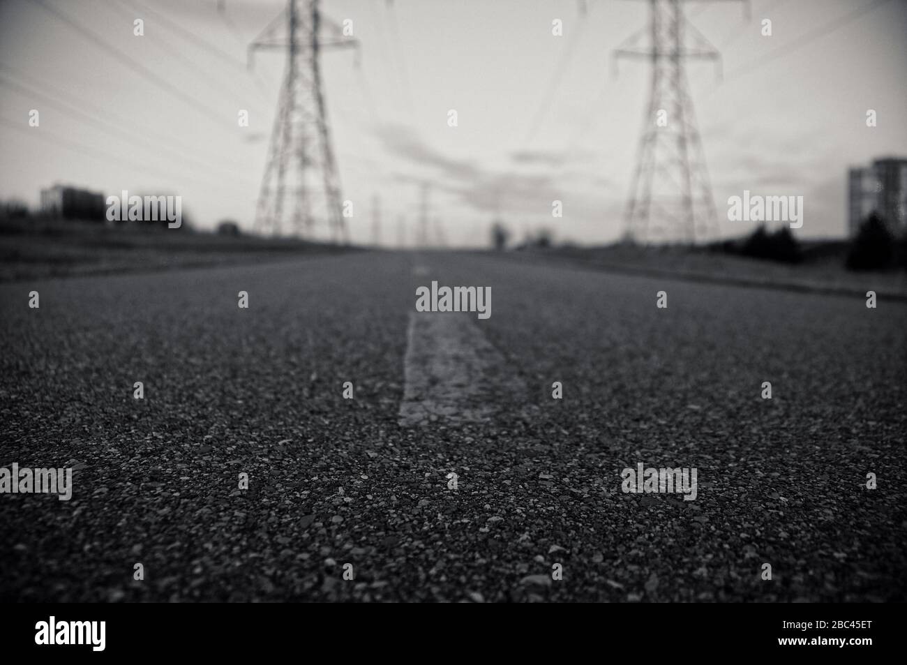 Nahaufnahme der schwarzen Asphaltstraße mit verblassten Strichlinien vor Hydropolen und trübem Abendhimmel Stockfoto