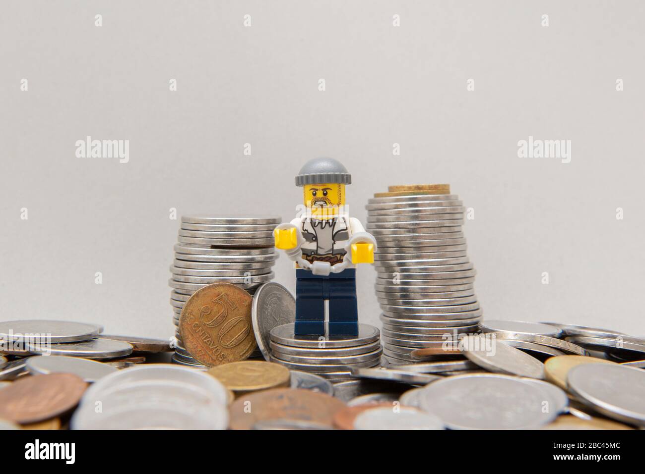 Florianopolis, Brasilien, 28. März 2020: Bandit Handschellen neben einem Stapel Münzen. Kriminalität zahlt nicht auf weißem Hintergrund. Bankraub. LEGO Minifigur Stockfoto