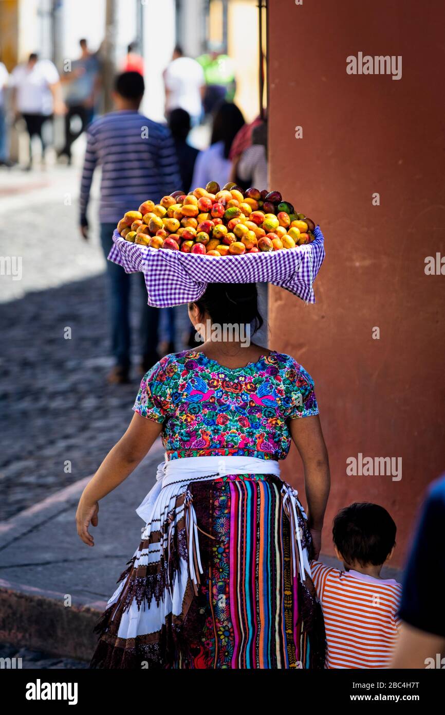 Eine Mutter trägt einen Obstkorb auf dem Kopf, während sie auf den Markt in Antigua, Guatemala geht. Stockfoto