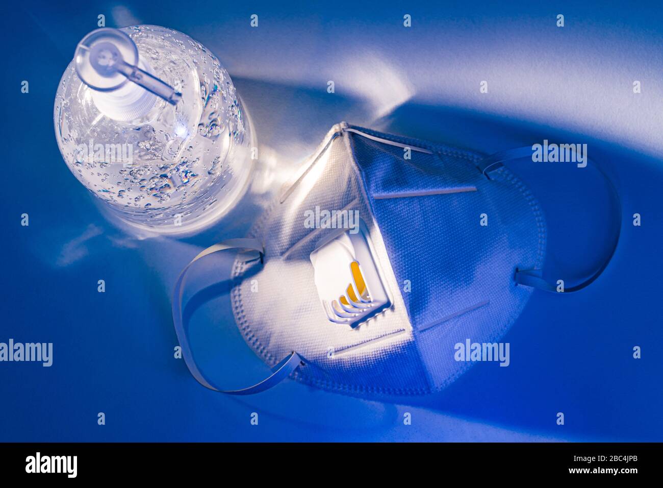 Antiseptisches Handgel und N95-Maske auf weißem Tisch mit dramatischem Lichteffekt, Gesundheitskonzept Stockfoto