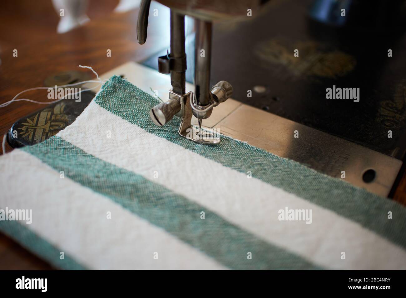 Nähen einer falten Stoffmaske aus einem grün-weiß gestreiften Geschirrtuch auf einer Antik-Sängerin 127 Nähmaschine Stockfoto