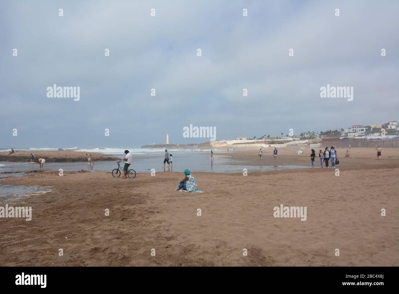 Die Einheimischen entspannen sich am öffentlichen Strand von Casablanca, Marokko, mit dem historischen Leuchtturm El Hank im Hintergrund. Stockfoto