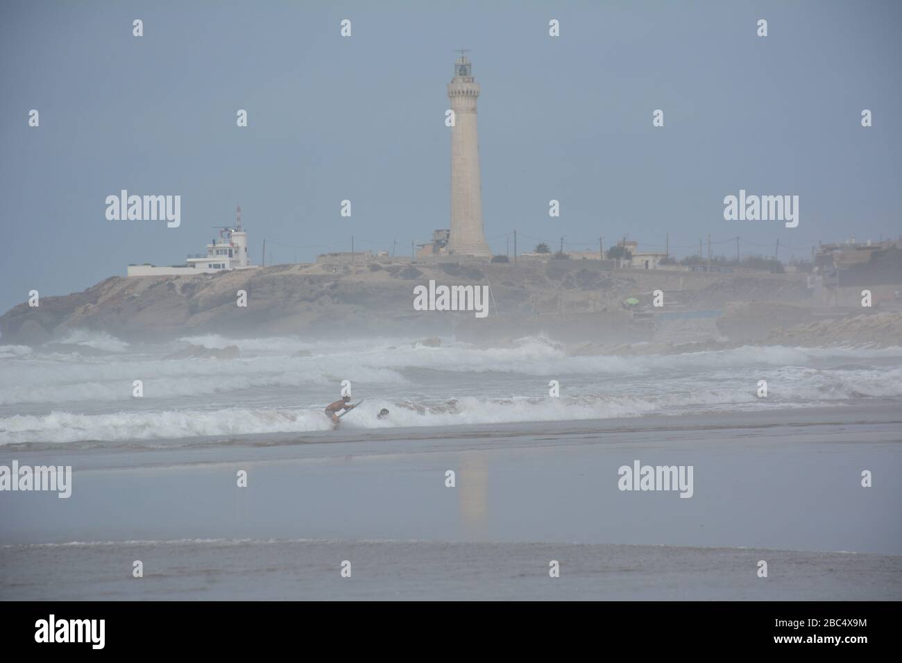 Am öffentlichen Strand von Casablanca, Marokko, mit dem historischen Leuchtturm El Hank, baden und spielen die Einheimischen im Meer. Stockfoto