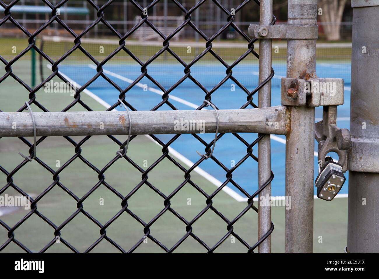 Nahaufnahme des mit einem Schloss gesicherten Tores eines Tennisplatzes mit Netz im Hintergrund. Stockfoto