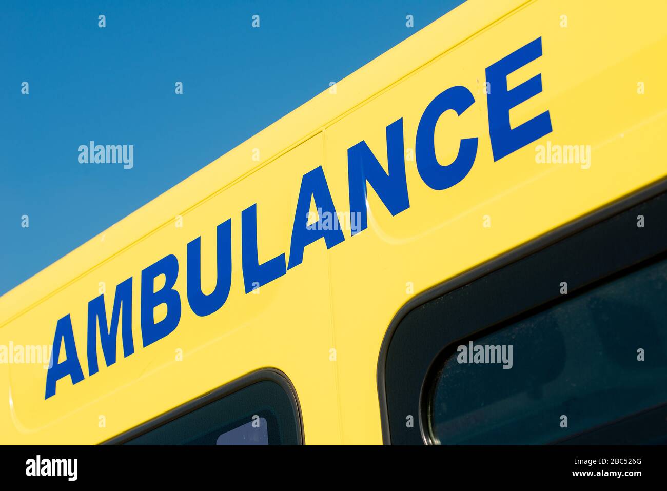 Niedriger Winkel des HINWEISSCHILDES DES RETTUNGSWAGENS auf gelbem NHS-Notarzteinsatzfahrzeug, mit hellblauem Himmel. Stockfoto