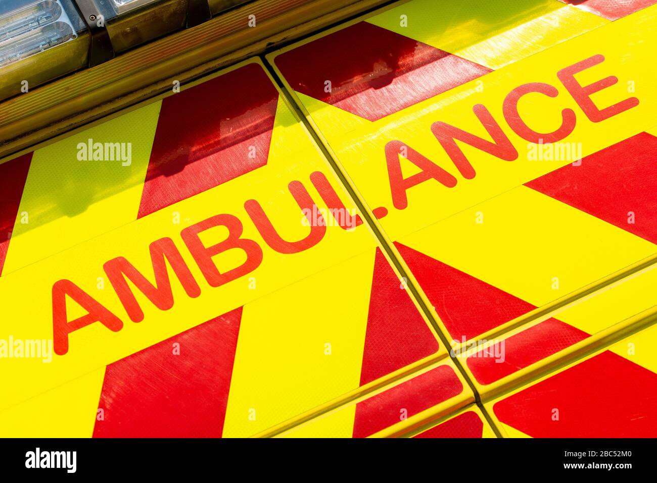 Dramatischer, abgewinkelter Blick auf das SCHILD FÜR DEN RETTUNGSWAGEN auf dem roten und gelben NHS-Notarzteinsatzfahrzeug. Stockfoto