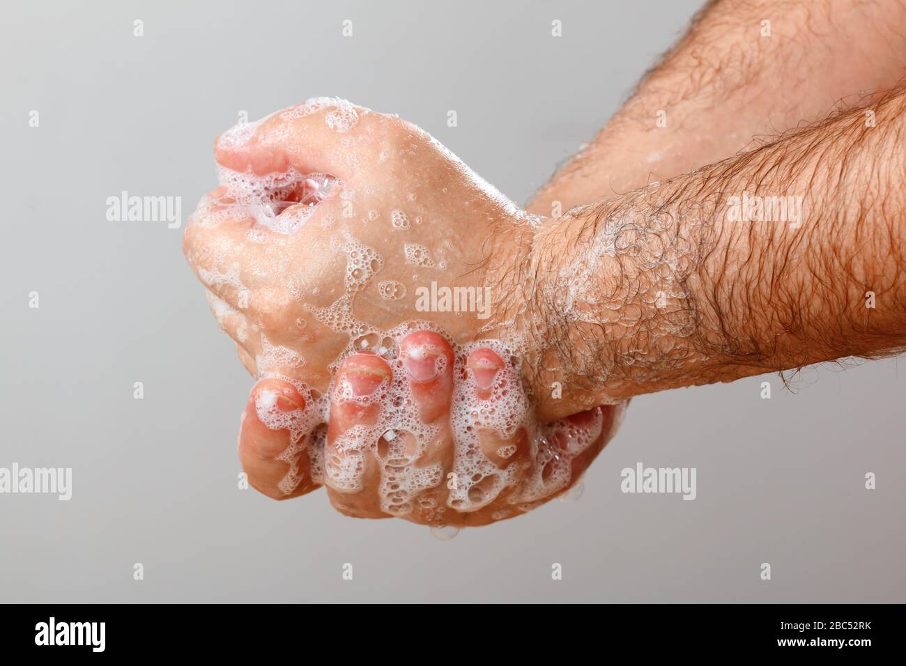Nahaufnahme eines Mannes, der die Hände mit Seife auf grauem Hintergrund waschen kann. Hygienische Vorbeugung gegen die Desinfektion des Coronavirus Virus. Stockfoto