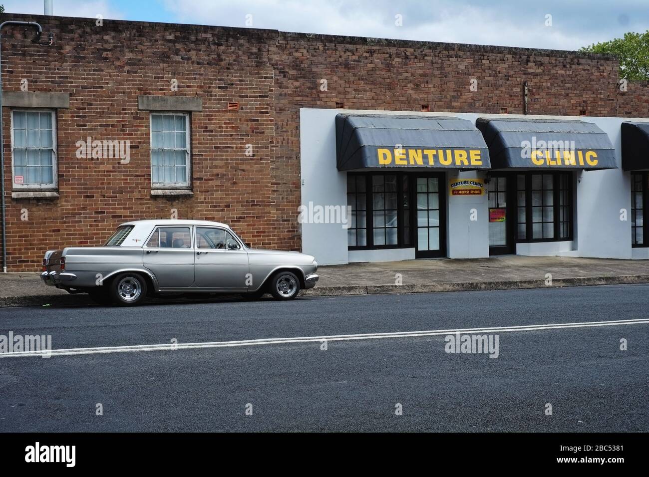 Der zweifarbige EH Holden Wagen aus Silber und Weiß, der auf der Straße geparkt ist, eine Ziegelwand und eine Klinik für Gebissschutz, in Mittagong, Southern Highlands, Australien Stockfoto