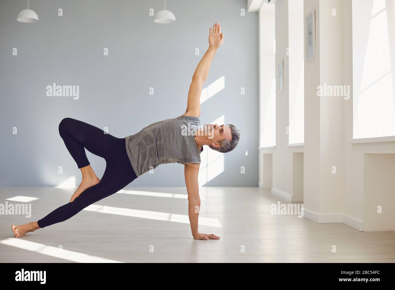 Yoga-Mann. Ein Mann in Sportswear übt auf dem Boden in einem grauen Raum Yoga-Balance aus. Das Konzept eines aktiven Lebensstils von Sport Sport Sport Yoga pi Stockfoto