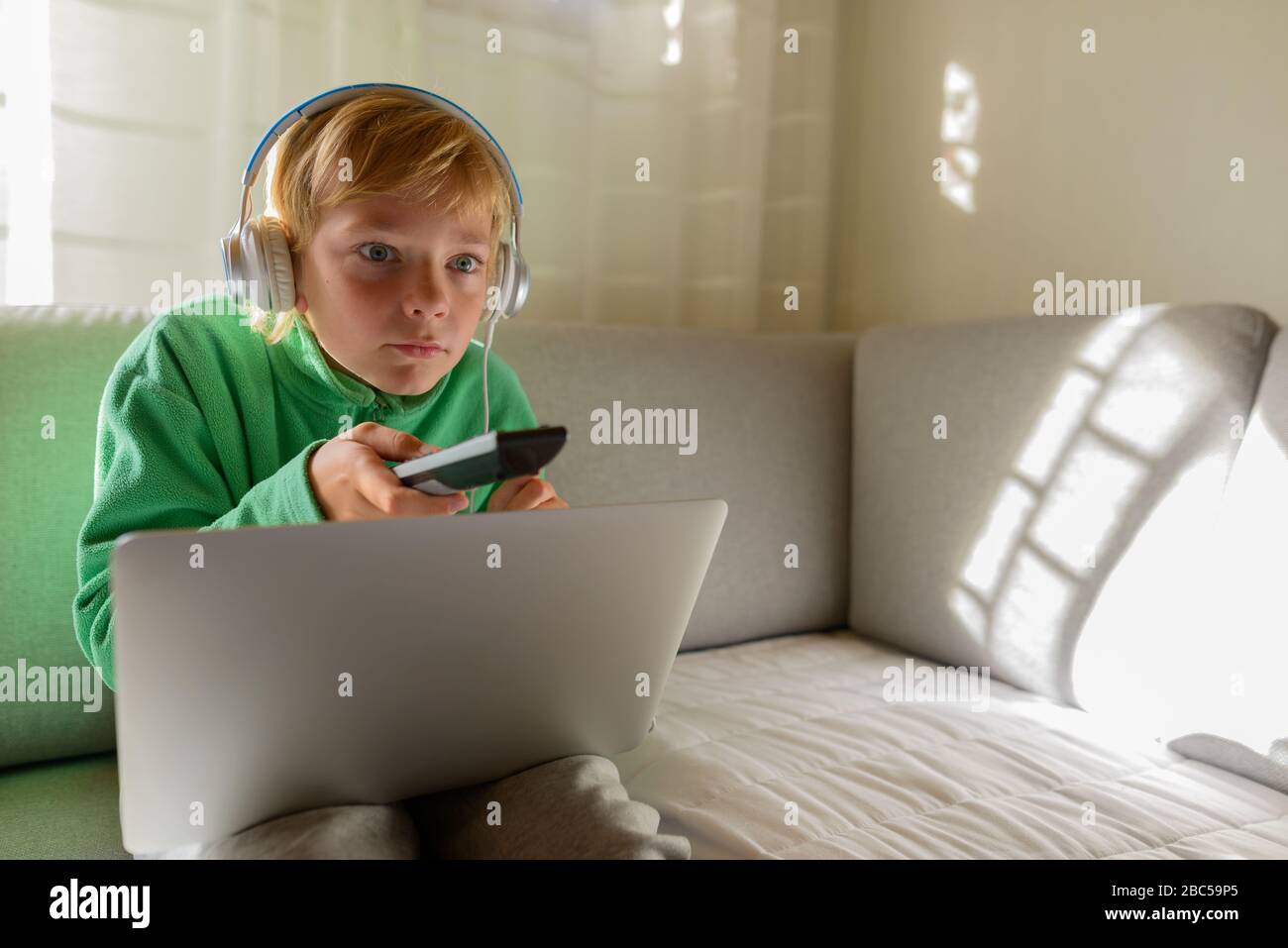 Kleiner Junge mit Kopfhörern und Laptop, der sich beim Fernsehen zu Hause fokussiert Stockfoto