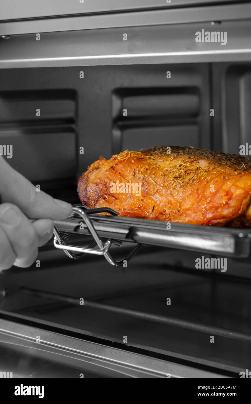 Mann, der ein Lammfund aus einem elektrischen Ofengrill nimmt. Mit selektiver Farbe Stockfoto