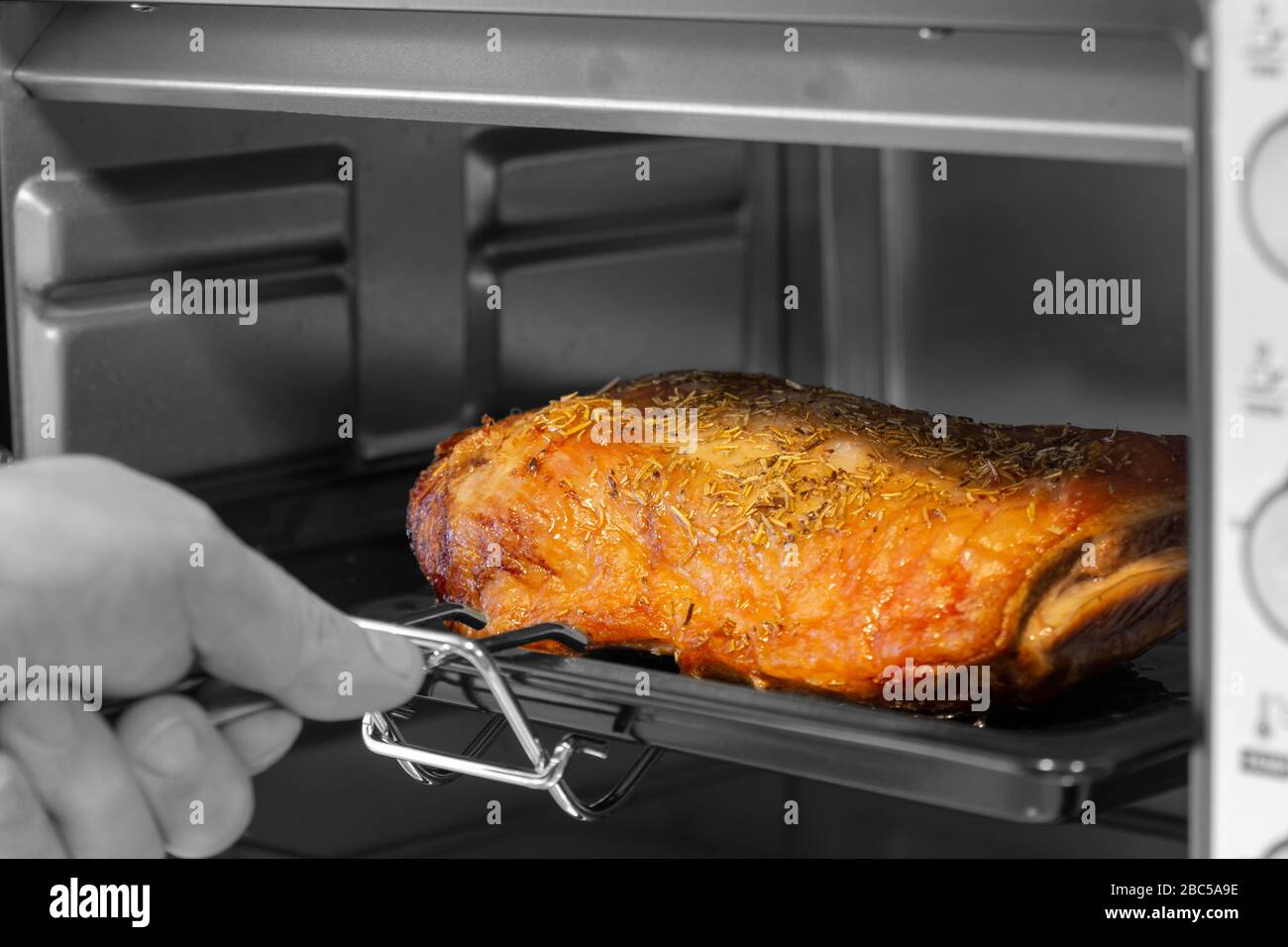 Mann, der ein Lammfund aus einem elektrischen Ofengrill nimmt. Mit selektiver Farbe Stockfoto