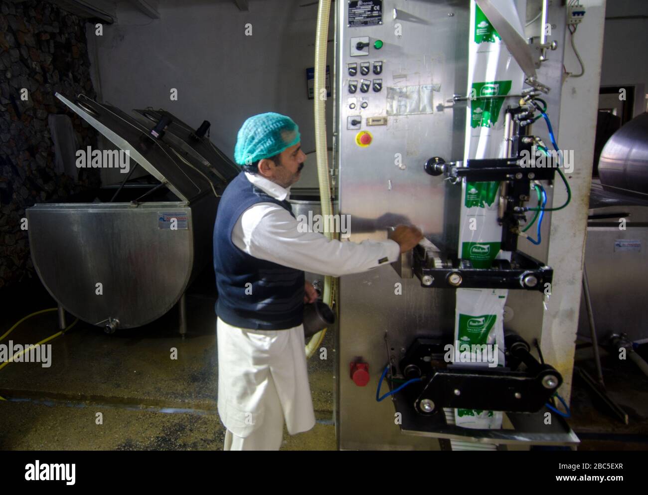 Ein Arbeiter, der die Milchlager- und Verpackungsmaschinen in einer Milchfarm in Nowshra, Pakistan betreibt. Stockfoto