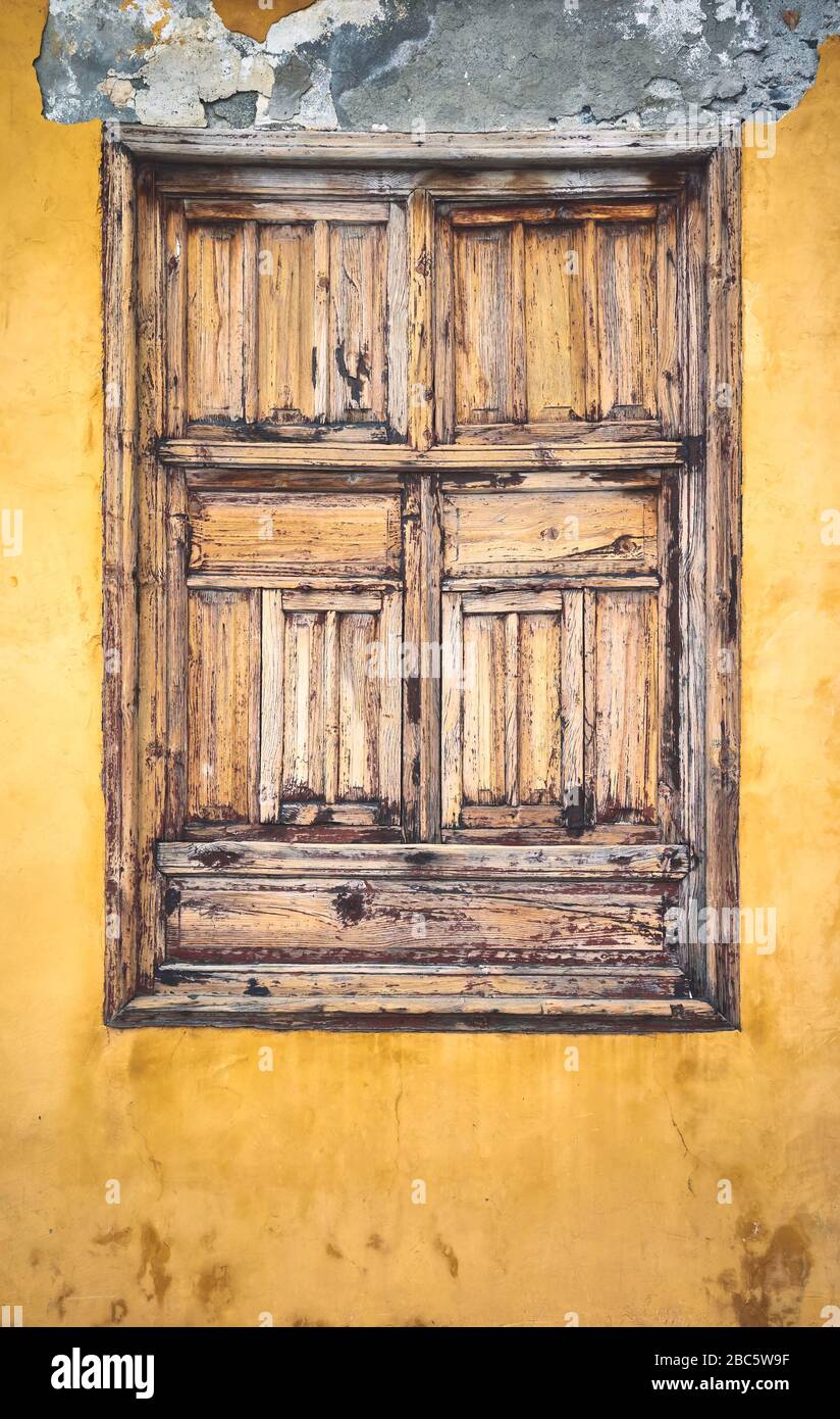 Altes geschlossenes Fenster aus Holz in gelb bemalter Wand. Stockfoto