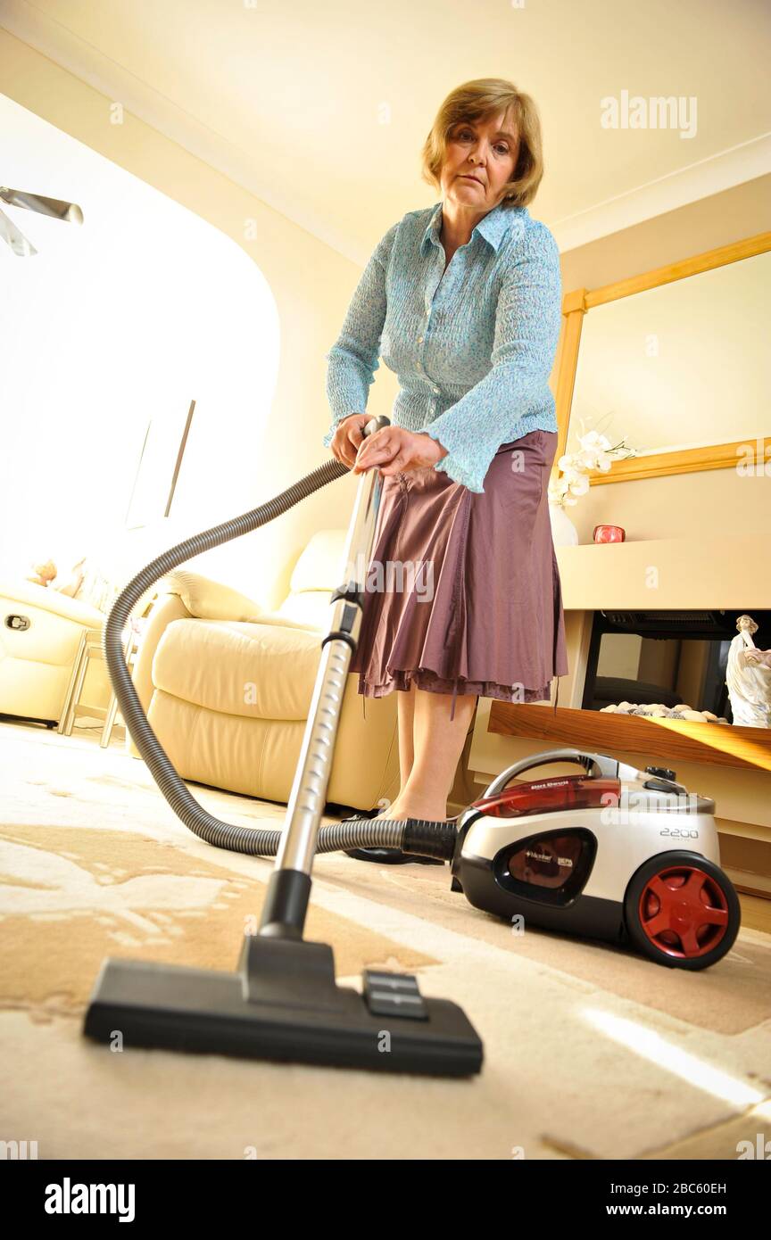 Ältere Frau saugt in ihrer Lounge zu Hause Staubsauger ab. Eine übermäßige Reinigung kann ein Zeichen für eine obsessive Zwangsstörung sein. Stockfoto