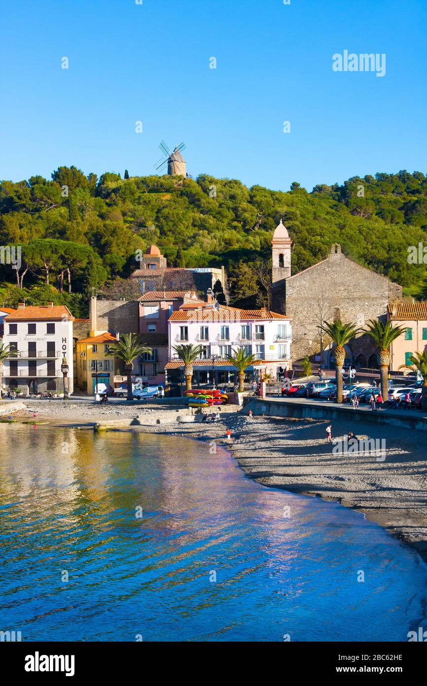 Collioure, Frankreich - 24. Februar 2020: Strandhotels in Collioure Village mit Windmühle auf Hügel, Roussillon, Vermilion-Küste, Frankreich. Es ist eine Oase der Künstler Stockfoto