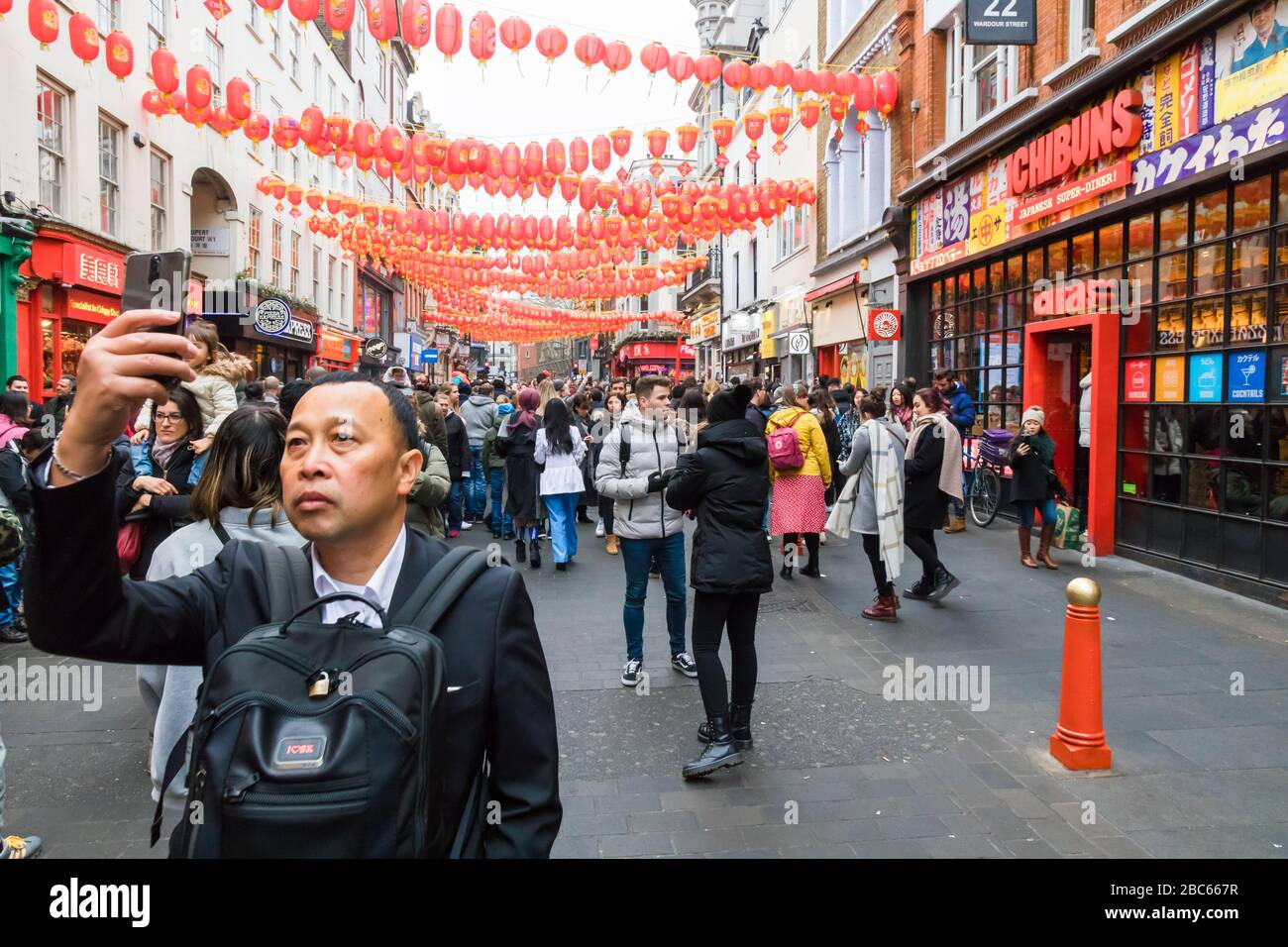 Asiatischer/orientalischer Mann, der selfie in belebter Straße fotografieren lässt, bei den chinesischen Neujahrsfeiern 2020 in Chinatown, London. Stockfoto