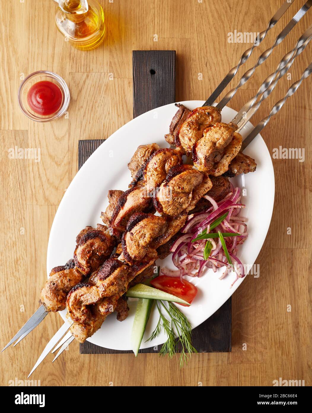 Traditionelle Schaslik auf einem Grillspieß in der Nähe von Tomatensauce und Öl auf schwarzem Holzbrett und Holzhintergrund Draufsicht Stockfoto