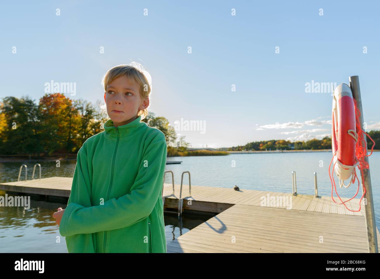 Junger gutaussehender Junge, der an einem Holzsteg in der Nähe des Flusses denkt Stockfoto