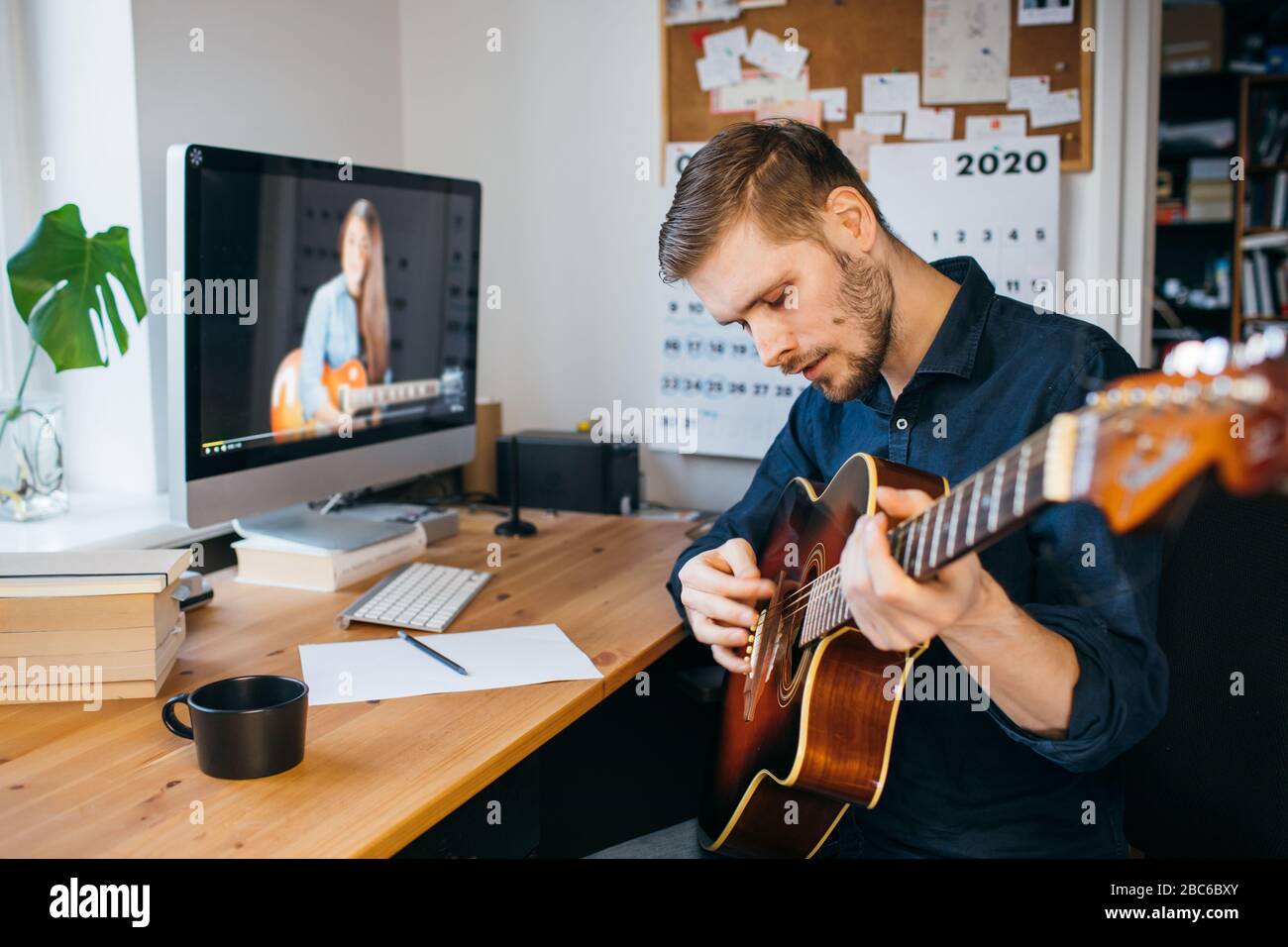 Mann lernen, wie man Gitarre aus Online-Tutorial spielen. Mann spielt akustische Gitarre. Bleib zu Hause Konzept während Coronavirus Pandemie. Stockfoto