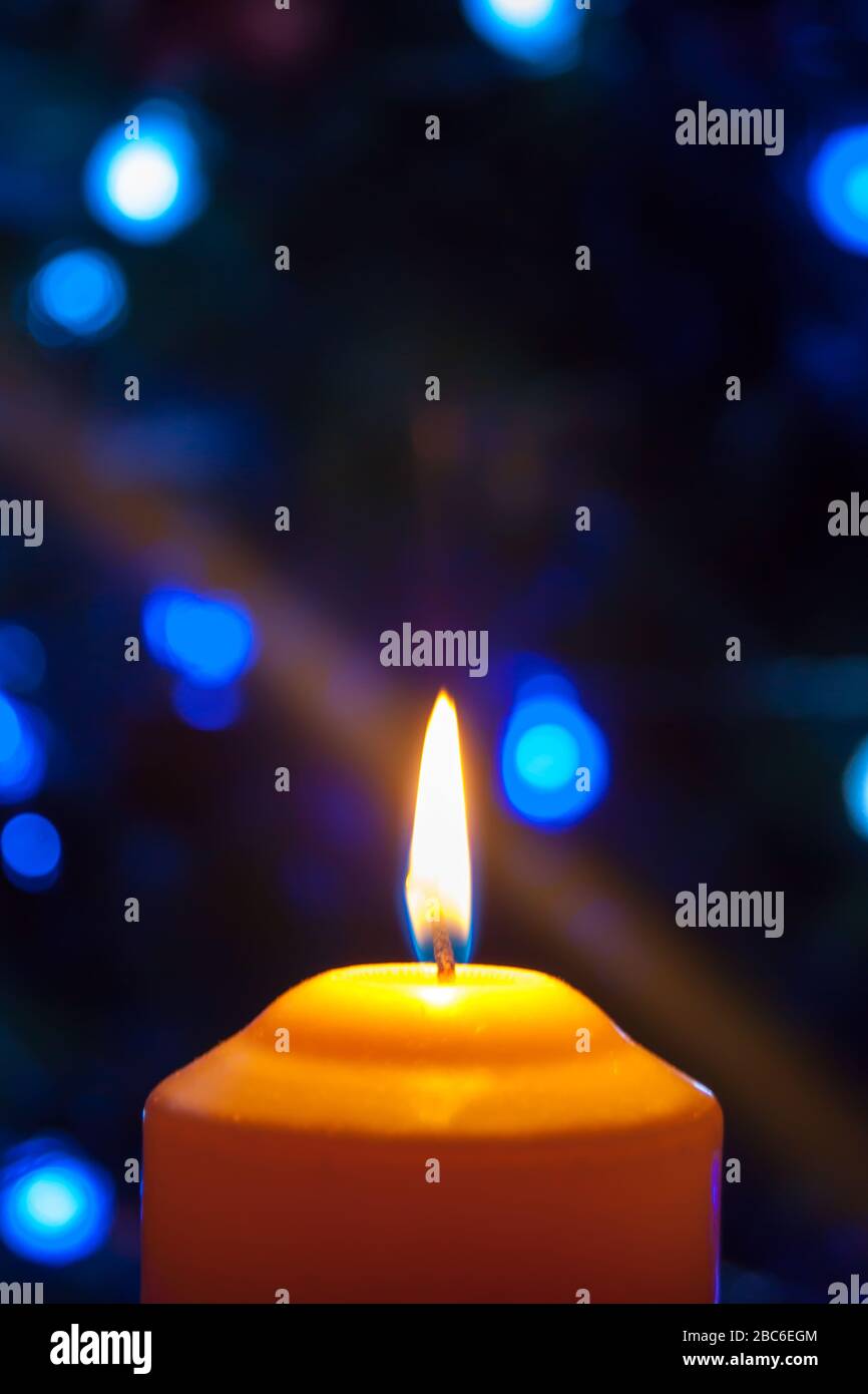 Eine große Kerze brennt vor dem Hintergrund einer Girlande mit strahlendem Licht. Vertikales Foto, Unschärfe. Mystische esoterische Romantik Divination Stimmung getauft Weihnachts-Karol-Setcer Stockfoto