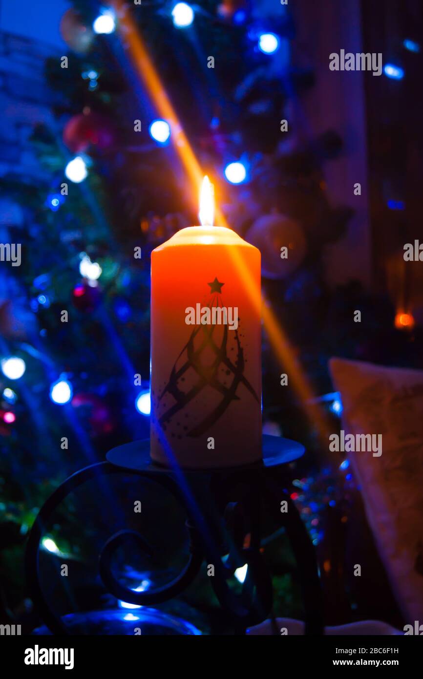 Eine große Kerze brennt vor dem Hintergrund einer Girlande mit strahlendem Licht. Vertikales Foto, Unschärfe. Mystische esoterische Romantik Divination Stimmung getauft Weihnachts-Karol-Setcer Stockfoto