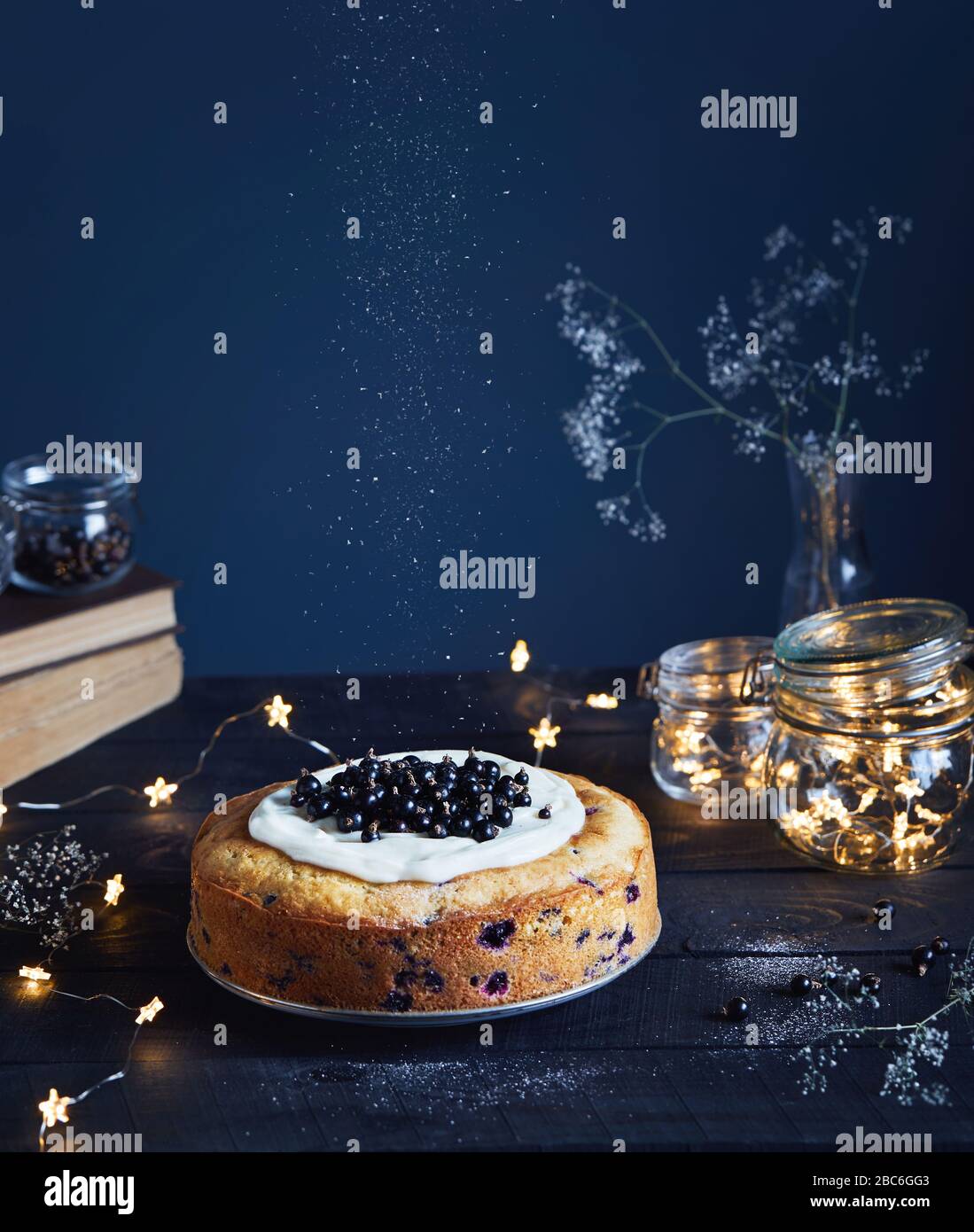 Hausgemachter Kuchen mit schwarzem Currant und Mascarpone auf dem Holztisch in der Nähe alter Bücher und Glasgefäße mit hellen Sternen auf dunklem Hintergrund im Sommer Stockfoto