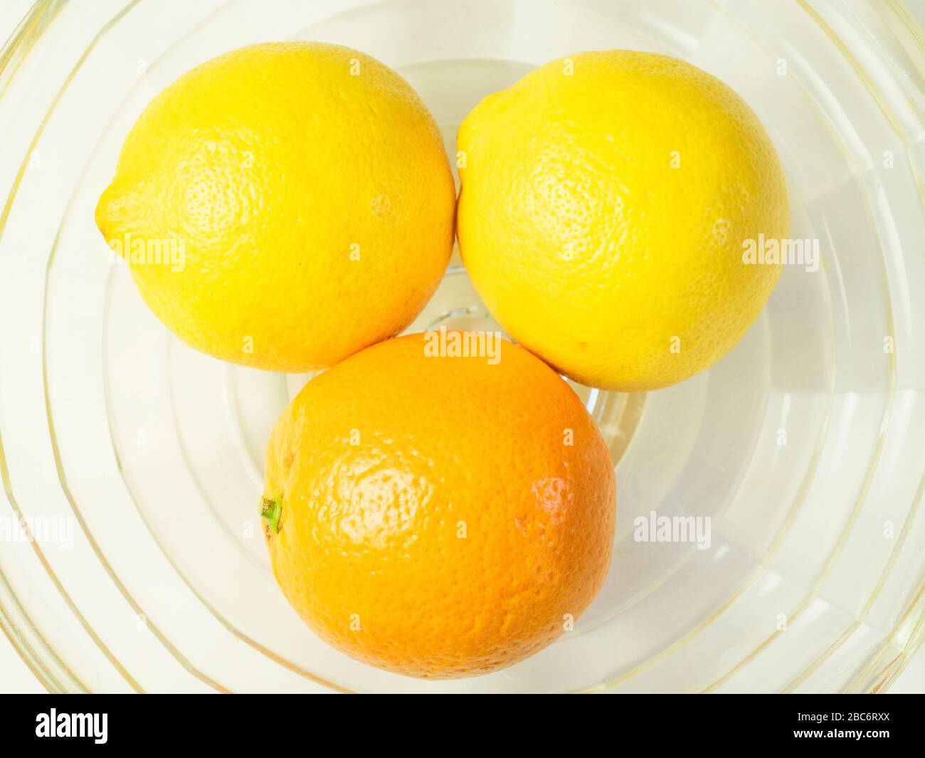 Eine orangefarbene und zwei Zitronen in einer gläsernen Fruchtschale Stockfoto