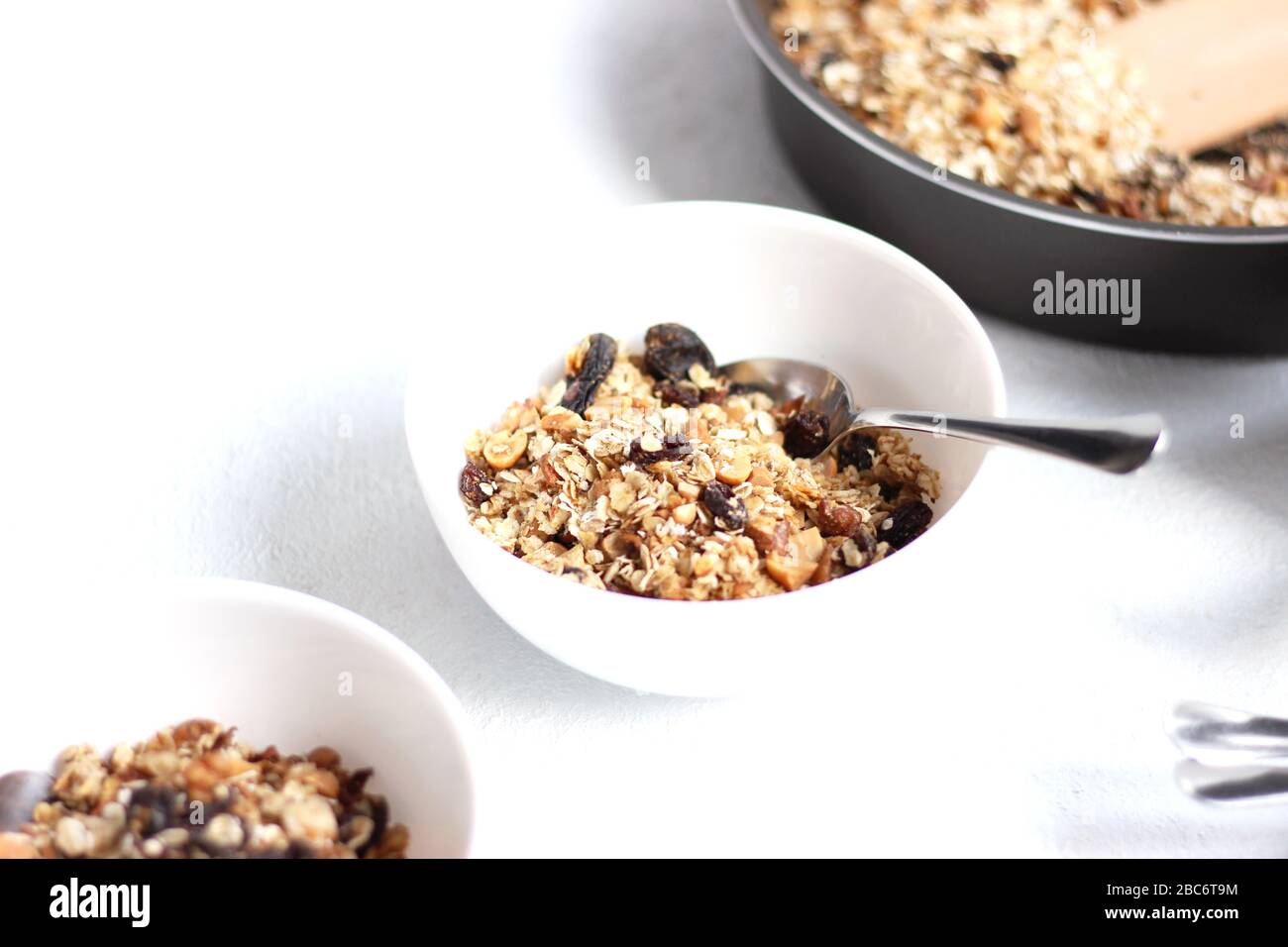 Tischeinstellung der Getreideschüsseln auf weißem Hintergrund. Frühstücksschüsseln mit Müsli und Nüssen und Rosinen. Konzept Für Gesunde Ernährung. Stockfoto