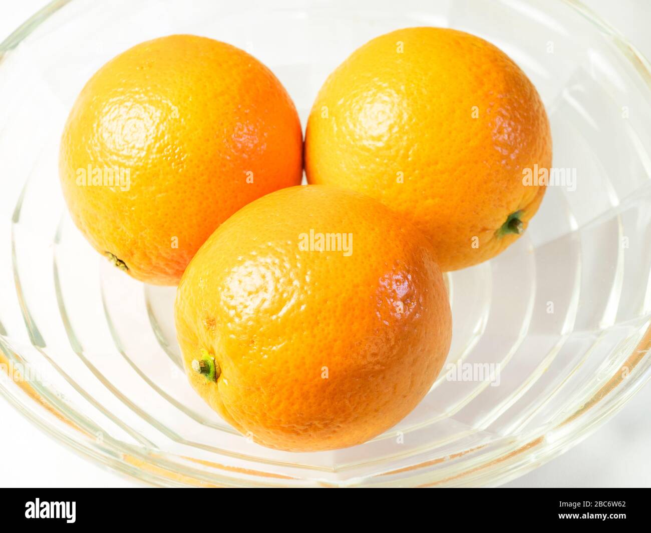 Drei Orangen in einer Glasschale auf einer weißen Tischdecke Stockfoto
