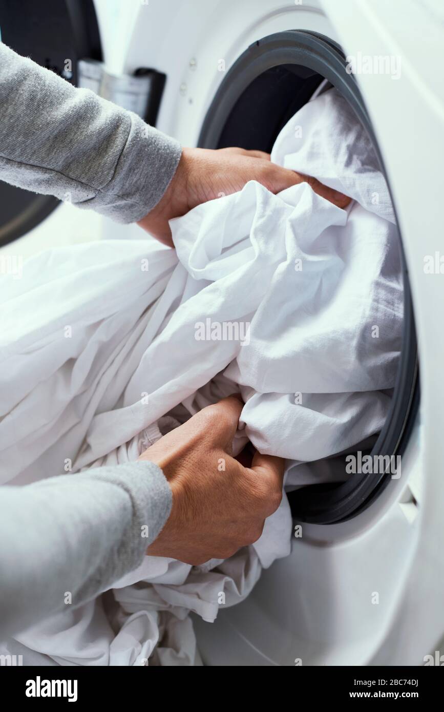 Nahaufnahme eines jungen kaukasischen Mannes, der weiße Bettwäsche in die Waschmaschine stellt Stockfoto