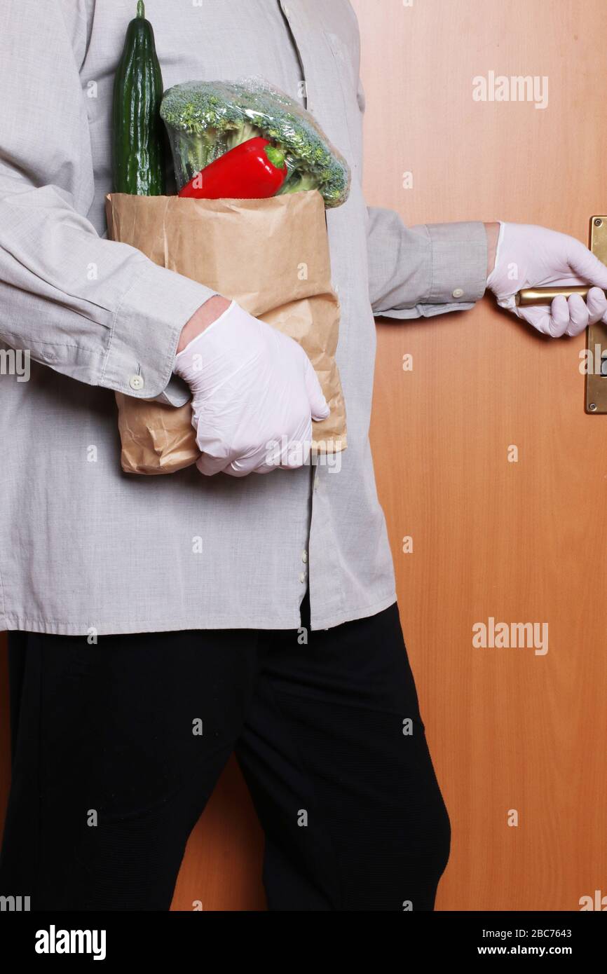 Ein Mann, der medizinische Handschuhe und eine Einkaufstasche mit frischem Gemüse trägt, betritt das Haus. Konzept der Stärkung des Immunsystems und des Schutzes Agai Stockfoto
