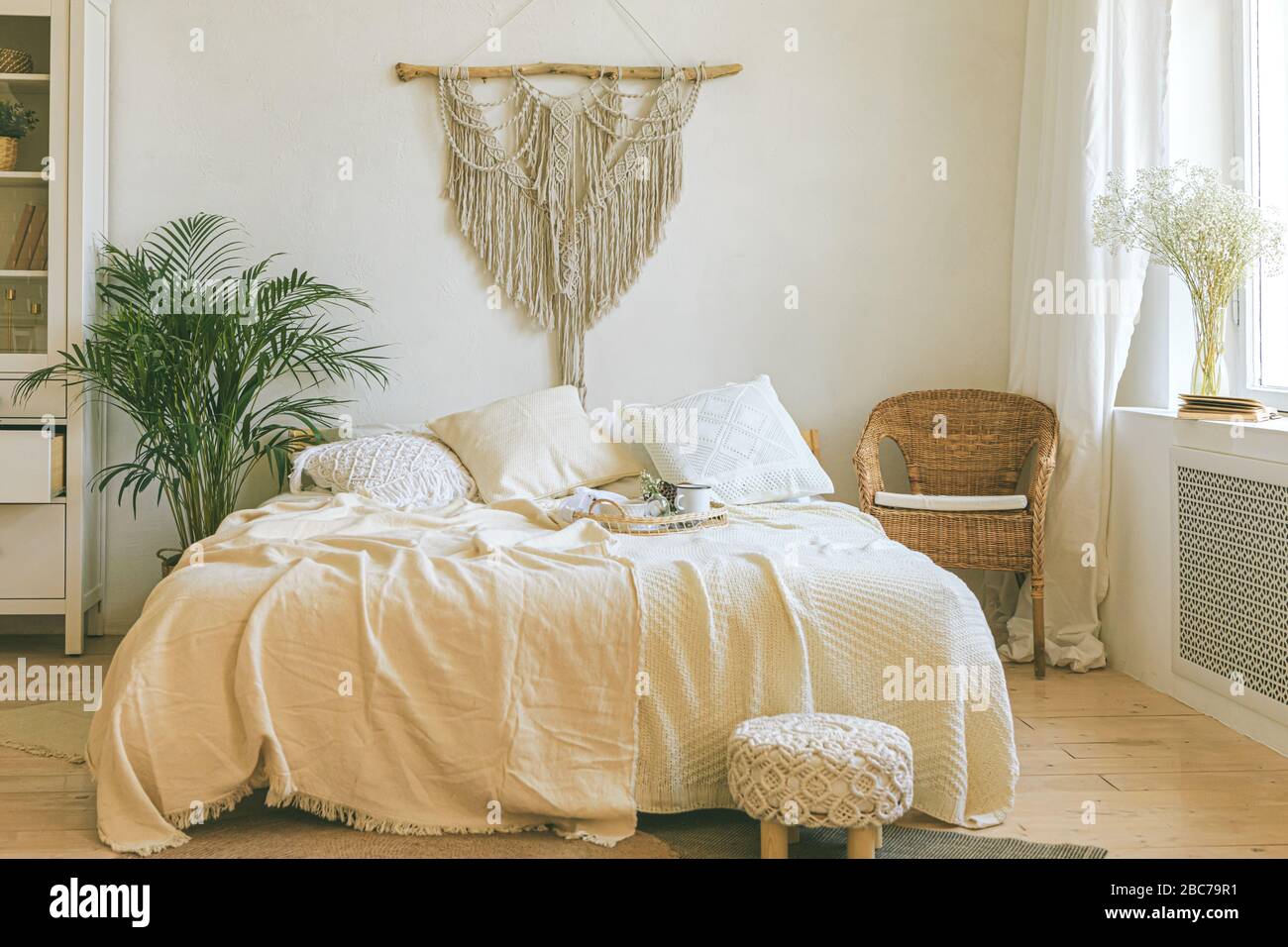 Modernes, romantisches zimmer im scandi boho Stil mit dekorativen Kissen, grüner Anlage und einer makramen Wandverkleidung. Leichtes, warmes, gemütliches, komfortables Zuhause Stockfotografie