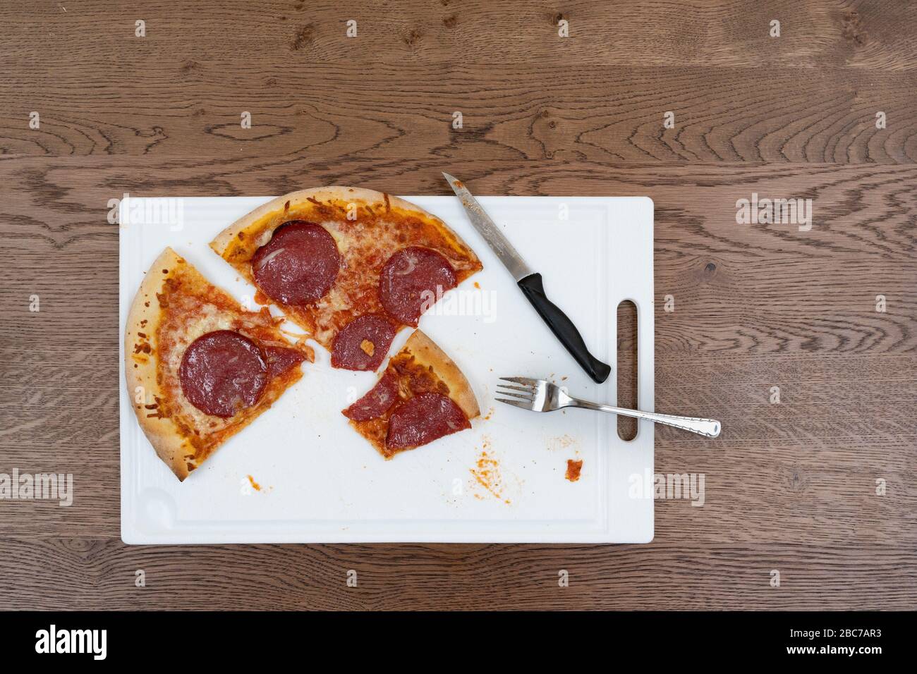 Eine Salami-Pizza wird während einer Mahlzeit auf einem weißen Schneidebrett geschnitten. Stockfoto